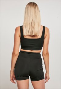 Crni sportski crop top i odgovarajuće visokotalične šortse. Glatka, rastezljiva tkanina s dizajnom kvadratnog izreza i minimalističkim stilom.