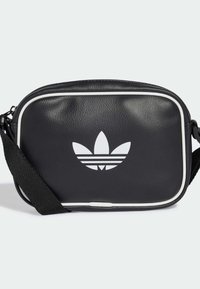 Čierna kožená crossbody taška s bielym lemovaním a veľkým bielym logom s tromi pruhmi. Obsahuje nastaviteľný čierny popruh. Obdĺžnikový tvar.