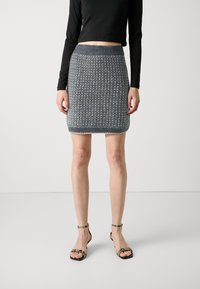 Pelēka adīta minisvārki ar faktūru, ribotām jostām un izsisto apakšmalu. Saskaņots ar melniem siksnu zābakiem.