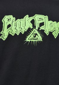 Sort bomulds t-shirt med fed grøn "Pink Floyd" tekst og et øje inden for en trekant design, med strålende linjer for at fremhæve.