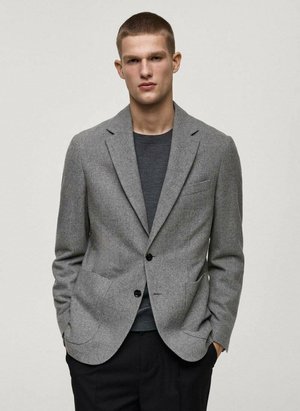 Gray blazer made from textured fabric, featuring notch lapels, two front pockets, and two black buttons. Worn over a dark grey shirt.