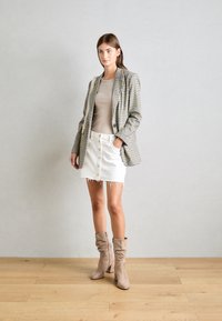 Blazer i grå och svart rutigt, beige topp, vit denimkjol med knappar och beige slouchy ankelskängor. Svala texturer och figurnära design.