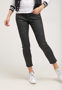 Svarta skinnyjeans i denim med ribbade knädetaljer och en smal passform, i kombination med vita sneakers och en randig bomberjacka.