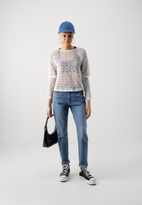 Hvit bluse med lange ermer i blonde med sirkulært mønster, lyseblå denimjeans, svarte joggesko og liten svart håndveske. Blå caps fullfører antrekket.