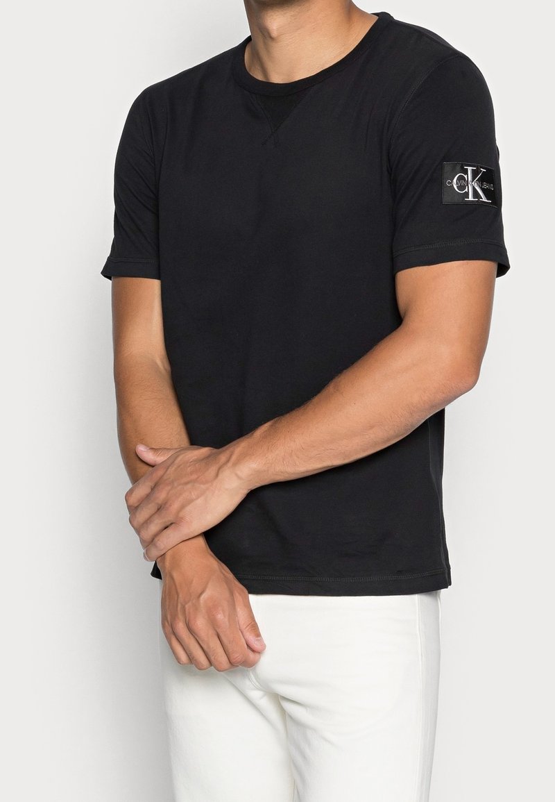 Černé tričko s krátkým rukávem vyrobené z bavlny s kulatým výstřihem. Na levém rukávu má nášivku s logem Calvin Klein a je tvarované.