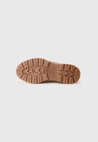 Brown rubber outsole with deep lugs for traction, featuring a round logo and crossed patterns. Smooth surface with a matte finish.