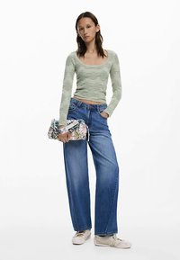 Ljusgrön texturerad långärmad topp, högmidjade blå vida jeans och en mönstrad clutchväska, bärs med beige slip-on skor.