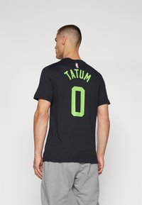 Must must black T-särk rohelise kirja "TATUM" ja numbri "0" tagaküljel. Särgil on lühikesed varrukad ja ümmargune kaelus.