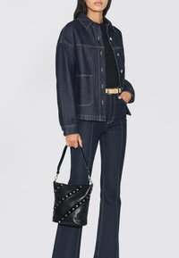 Chaqueta de mezclilla oscura con costuras claras, combinada con jeans oscuros de cintura alta. Sosteniendo un bolso tipo cubo de cuero negro con tachuelas plateadas.