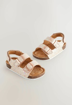 Blizgučios auksinės šlepetės su trimis reguliuojamais dirželiais, minkštu rudu zomšiniu padu, kontrastinga tamsiai ruda šsole ir baltu guminiu padu.