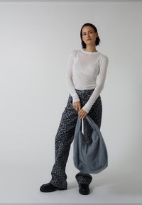 Baltas permatomas ilgomis rankovėmis viršus, pilkos spalvos plačios kelnės su leopardų raštu, juodi masyvūs batai ir pilka aptempta rankinė. Lygios medžiagos ir laisvas siluetas.