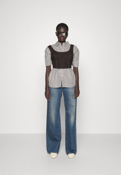 Chemise rayée à manches courtes avec un gilet marron contrastant, associée à un jean bleu à jambes larges et des baskets beiges ; lunettes de soleil noires élégantes.