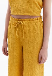 Ensemble deux pièces texturé jaune comprenant un top court et un pantalon à jambes larges. Les pantalons ont une taille élastique et un cordon de serrage ajustable.