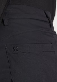 Pantaloni din țesătură neagră cu un design elegant, textură netedă și un mic logo brodat în formă de inimă pe buzunarul din spate.