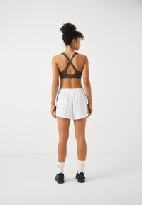 Sports-bh i mørk oliven med et utskåret bakstykke, paret med hvite shorts med elastisk midje. Sorte treningssko og hvite sokker fullfører looken.