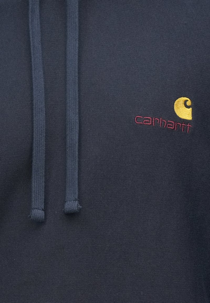 Marineblauwe hoodie van gestructureerde stof, met een capuchon met trekkoord en een geborduurd geel en bordeauxrood Carhartt-logo op de borst.