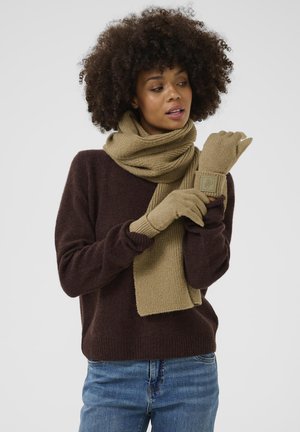 Brauner Strickpullover, olivgrüner Schal und passende Handschuhe mit strukturiertem Stoff. Die Handschuhe haben ein Patch-Detail am Handgelenk. Jeans sind sichtbar.