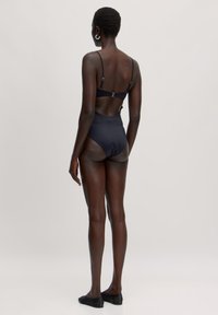 Zwarte eenpiece badpak met verstelbare bandjes en uitsnijding aan de achterkant. Glad materiaal, middellange pijpen, minimalistisch ontwerp.