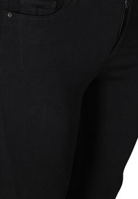 Jean en denim noir avec une coupe ajustée, poches visibles et un détail de fermeture éclair sur le côté, texture lisse et coutures minimales.