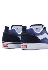 Paire de baskets Vans basses en suède bleu marine et blanc vues de dos, montrant des semelles blanches avec des logos rouges "Off The Wall".