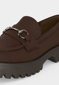 Σκούρο καφέ loafer με ασημένια λεπτομέρεια horsebit και χοντρή, ραβδωτή σόλα σχεδιασμένη για πρόσφυση και στυλ.