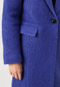 Purple wool coat with a textured finish, single button closure, and a side pocket, featuring a tailored fit and straight sleeve design.