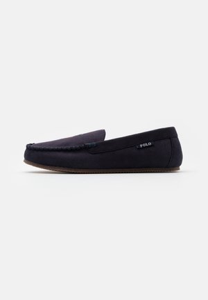 Mocassin homme en daim bleu marine foncé avec détail cousu sur la pointe, semelle plate marron et petite étiquette "Polo" sur le côté.