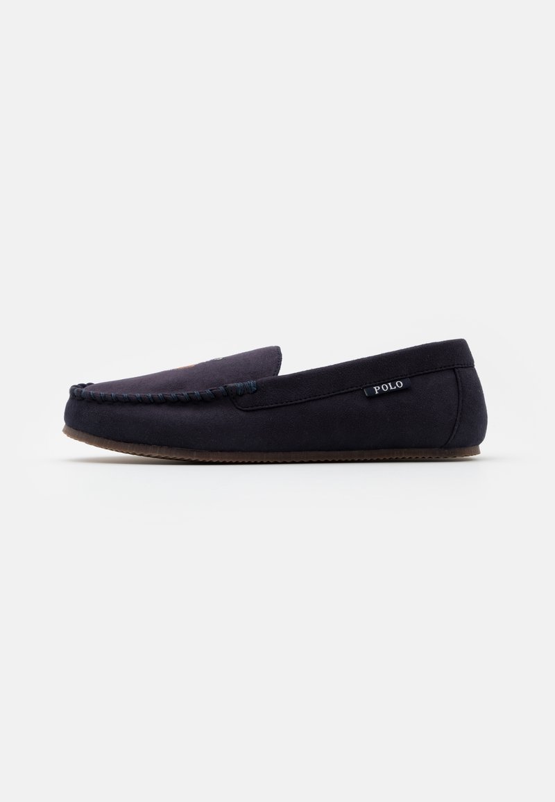 Mocassin homme en daim bleu marine foncé avec détail cousu sur la pointe, semelle plate marron et petite étiquette "Polo" sur le côté.