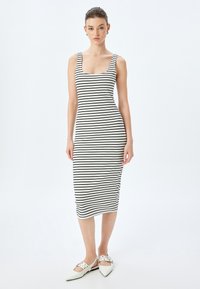 Gestreepte midi-jurk in zwart en wit, gemaakt van rekbare stof, met brede schouderbanden en een aansluitende silhouet. Draagt met puntige witte ballerina's.