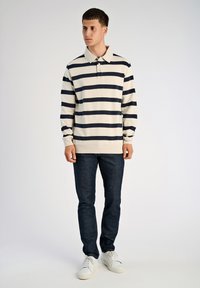 Koszulka polo z długim rękawem w kolorze kremowym z granatowymi poziomymi paskami, z kołnierzykiem i plisą, zestawiona z ciemnymi dżinsami i białymi trampkami.