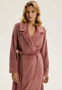 Różowy pluszowy szlafrok z wzorzystą teksturą i kołnierzem szalowym, z długimi rękawami i związanym paskiem w talii. Miękki, gruby materiał.