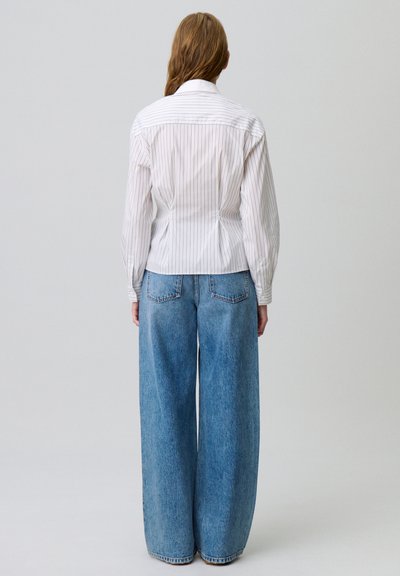 Camicia bianca a righe con vita aderente, maniche lunghe e colletto con bottoni, abbinata a jeans in denim blu a vita alta e taglio ampio.