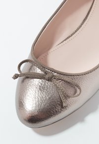 Ballerines métalliques rose doré avec une surface texturée, un bout arrondi et un accent en ruban en tissu fin à l'avant. Doublure intérieure lisse.