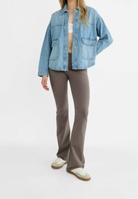 Lichtblauwe spijkerjas met een kraag, voorzakken en een relaxte pasvorm. Gecombineerd met bruine flare broeken en witte sneakers.