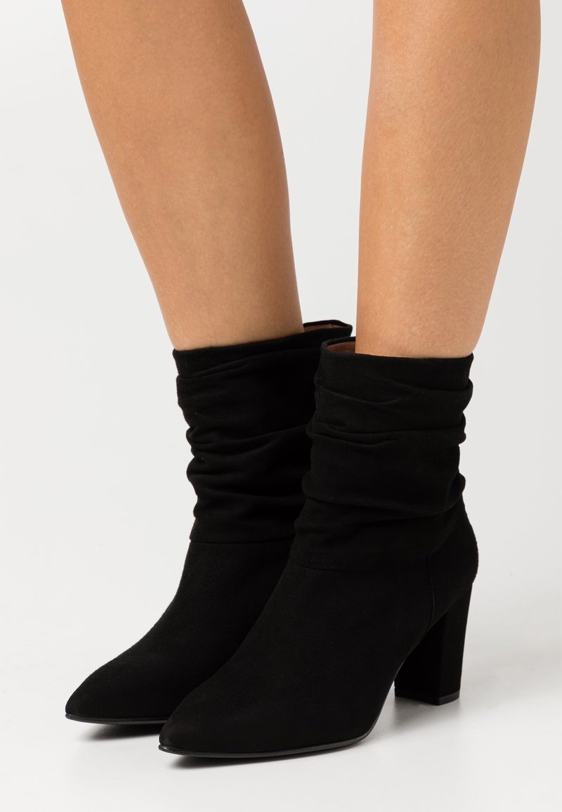 Stivaletti alla caviglia in suede nero con gambale morbido, punta a mandorla e tacco a blocco. La texture è morbida e opaca, senza elementi metallici visibili.