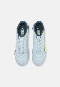 Scarpe da calcio sintetiche di colore azzurro chiaro con una parte superiore texturizzata, bordi blu scuro a contrasto e un accento verde lime lungo il lato.