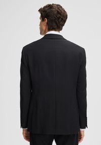 Giacca da abito nera con finitura testurizzata, spacchetto singolo sul retro e vestibilità sartoriale. Presenta bottoni sui polsini e rever a punte.