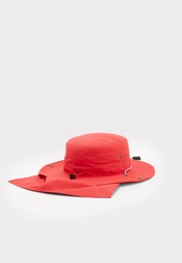 Chapeau imperméable rouge à large bord, avec cordon de serrage ajustable et fermetures à pression. Tissu léger avec une texture lisse.