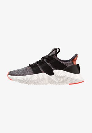 Baskets basses de sport avec tige en maille grise, brides noires, lacets noirs, semelle blanche texturée et accents orange au talon et aux orteils.