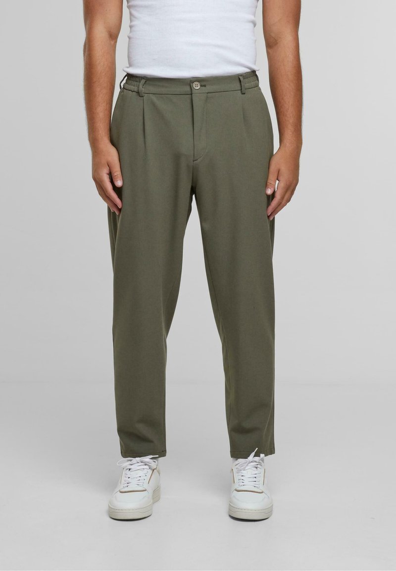 Pantalons vert olive avec une coupe droite, dotés d'une fermeture à bouton et d'une taille élastique, associés à des baskets blanches. Texture lisse.