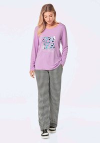 Lila Langarmshirt mit grafischem Design, kombiniert mit schwarz-weißen Hahnentritthosen und schwarzen Sneakern.