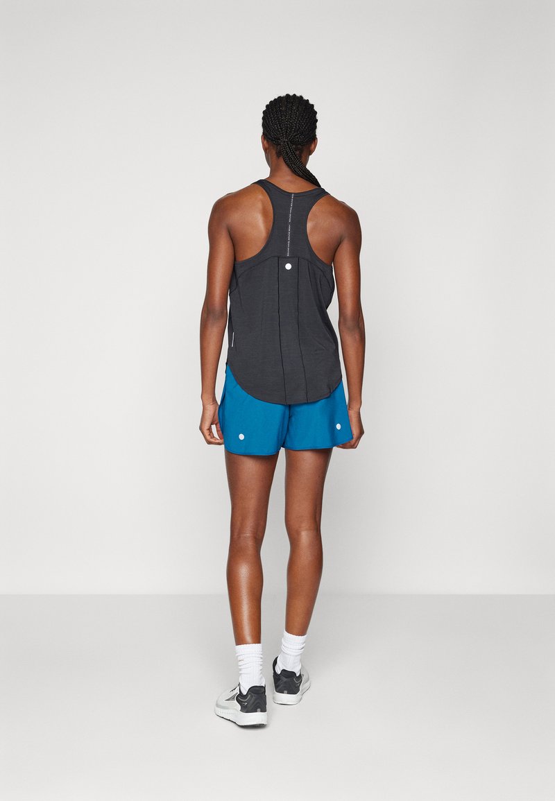 Débardeur de sport noir avec un design dos nageur, associé à un short bleu avec des accents blancs. Le modèle est de dos par rapport à l'appareil photo.