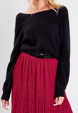 Maglione nero a maglia con design off-shoulder abbinato a una gonna plissettata con motivo floreale rosa intenso e una cintura nera con borchie.