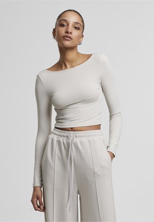 Dlhý rukáv, svetlo béžový crop top vyrobený z hladkej elastickej látky, skombinovaný so svetlo béžovými nohavicami vo voľnom strihu s elastickým pásom.