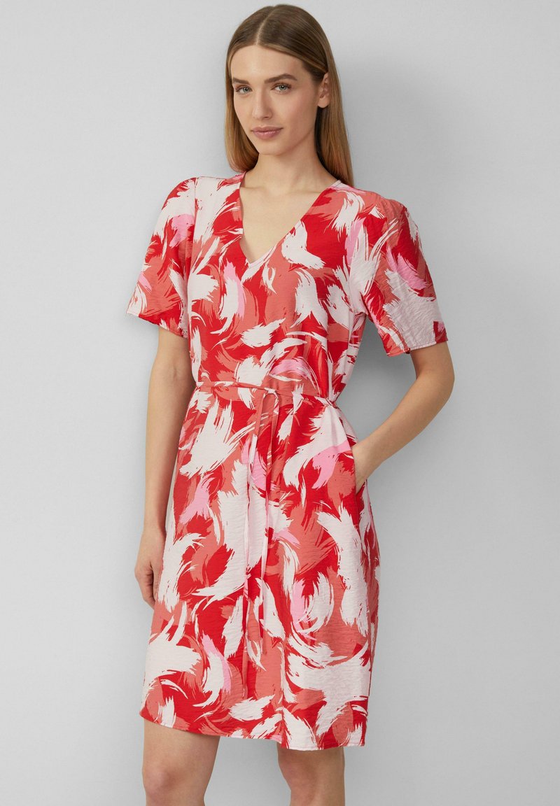 Robe à motif floral rouge et rose, avec des manches courtes, un col en V, une taille ceinturée et des poches. Le matériau semble léger et texturé.