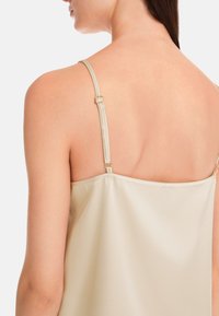 Cremefarbiges Satin-Camisole mit Spaghetti-Trägern und dezentem Glanz, verstellbarem Ringbeschlag an den Trägern und lässiger Passform.
