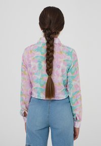 Camicia a maniche lunghe e corte in colori pastello con motivo tie-dye; presenta un colletto e polsini con bottoni. Abbinata a jeans a vita alta.