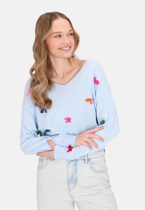 Jasnoniebieski, oversize sweter z dekoltem w kształcie litery V, ozdobiony kolorowymi kokardami z materiału w odcieniach różu, pomarańczy, zieleni i niebieskiego na przodzie i rękawach.