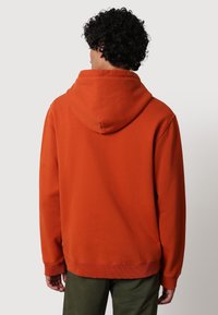 Oranžová bavlněná mikina s kapucí, která má velkou kapuci, žebrované manžety a lem, hladkou texturu a volný střih, pohled zezadu.
