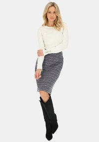 Biała, prążkowana bluzka z długim rękawem z guzikami, w połączeniu z dopasowaną granatową spódnicą o falistym, teksturowanym wzorze oraz czarnymi botkami do kolan.